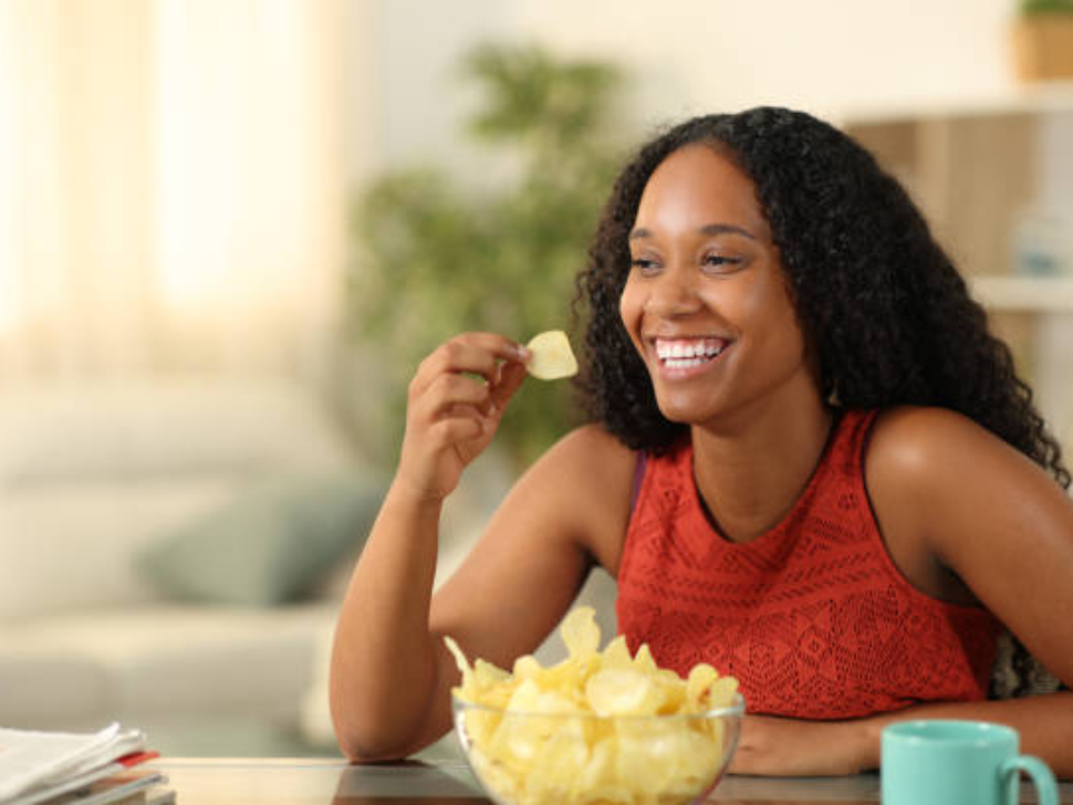 Happy black woman eating potato chips at home